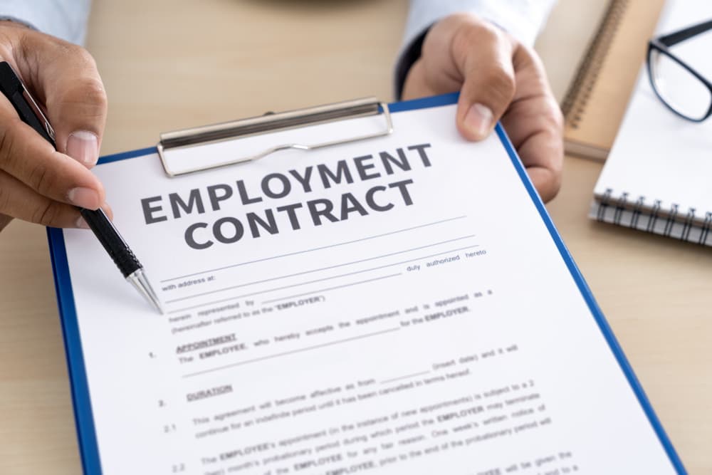 A professional signs an employment contract, symbolizing the successful completion of a job deal. The image captures the recruitment concept, with a close-up of the hand holding a pen poised over the document, ready to finalize the agreement.

