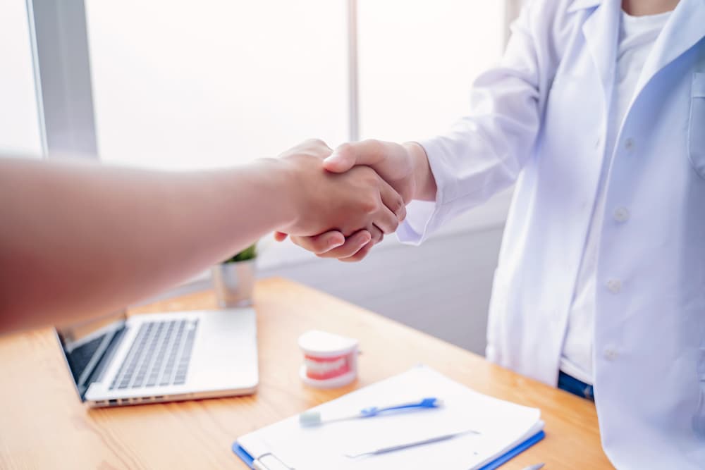 Female Dentist and Asian Businesswoman shaking hands up close.