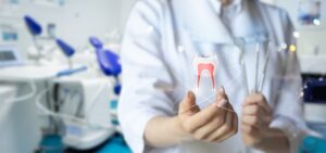 The dentist holds an instrument to display a tooth against a blurred background.