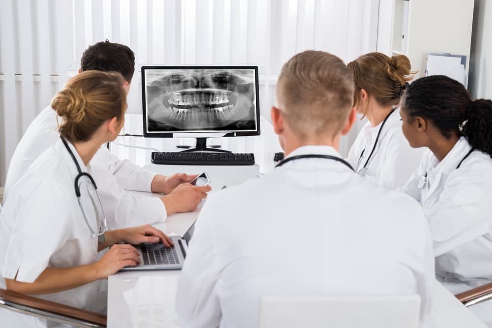 Group of doctors examining a teeth X-ray on a computer screen in a hospital.