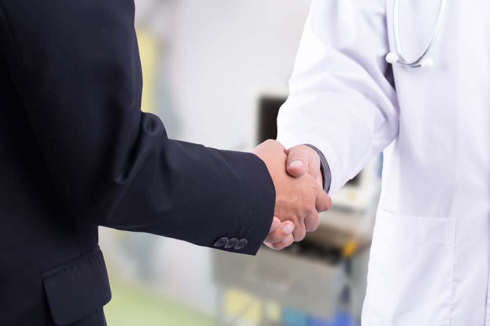 Doctor and businessman shaking hands in a hospital.