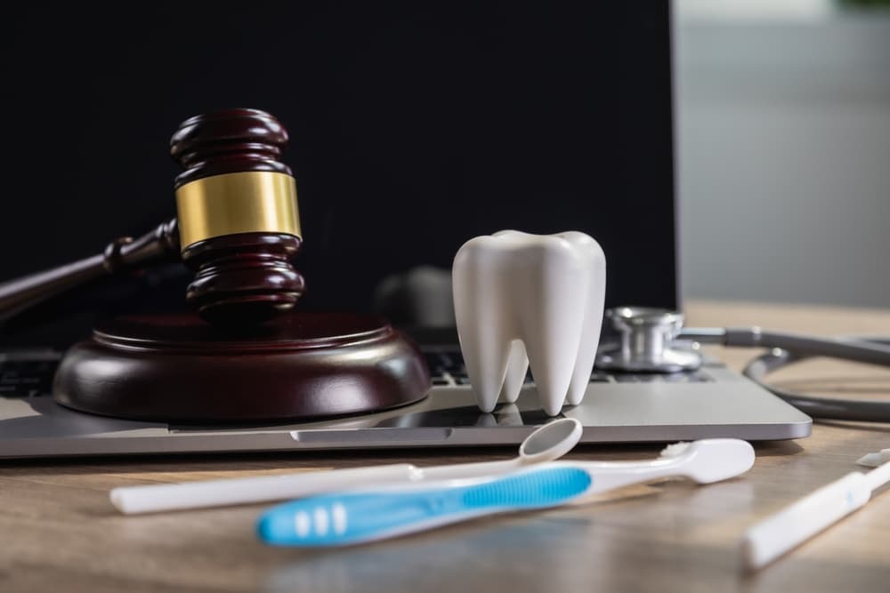 Dental tools and a gavel rest on a laptop, symbolizing the intersection of legal support and dental practice management