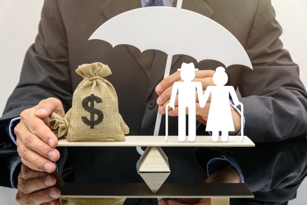 Senior couple standing on a seesaw or balance scale, representing pension insurance for retirees. One side features a bag of US dollars, symbolizing financial security, while the other side is shielded by an insurance provider, illustrating the concept of social security tax and financial protection for seniors.