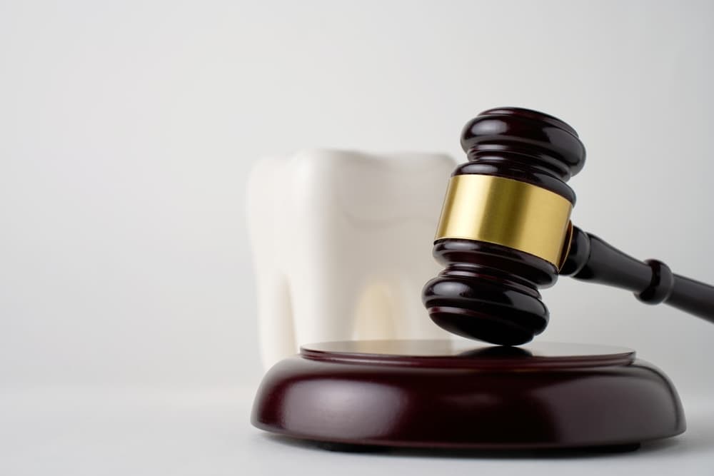 Image depicting a white tooth next to a judge's gavel, representing the concept of dental insurance and forensic dentistry or odontology.