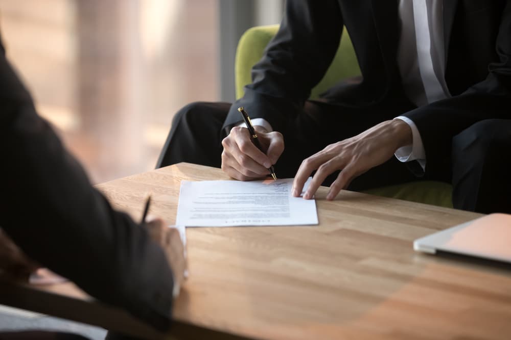 Close-up of businessmen signing a partnership agreement, with hands visible as they put signatures on an official paper document, symbolizing a formal business deal.