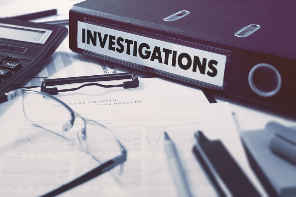 Ring Binder with inscription Investigations on Background of Working Table with Office Supplies, Glasses, Reports.
