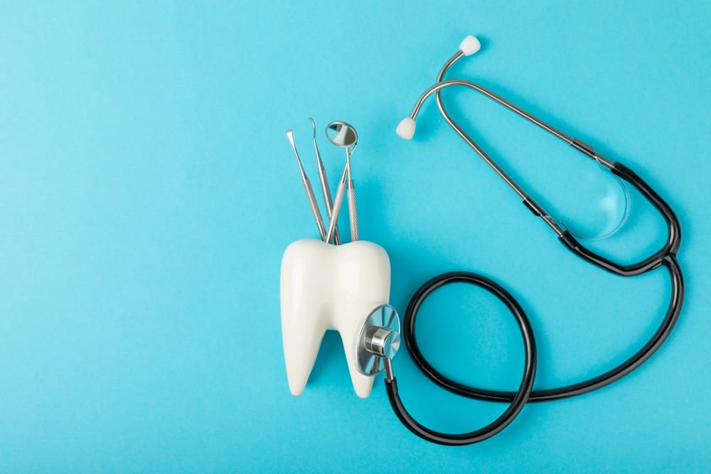 Tooth model with dental instruments and a stethoscope on a blue background, symbolizing dental practice operations and shared clinical responsibilities.